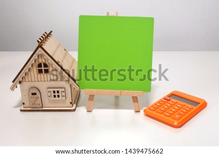 A miniature house, empty mini board and calculator. It is for property and finance purpose.