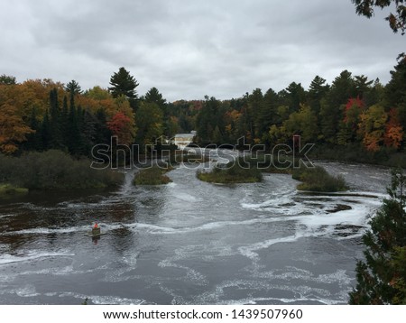Tahquamenon Falls in Upper Michigan Peninsula during Autumn showcasing fall colors. Photo captures green, yellow, orange and red color. Calm and serene environment. River gets quite after the falls.