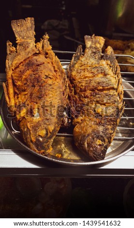 Aerial shot of two fried fish at a market stall on a dark background out of focus