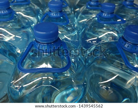 Large transparent plastic bottles without labels, filled with liquid arranged in rows.