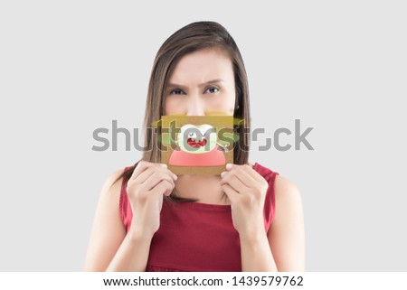 Asian woman in the red shirt holding a brown paper with the yellow teeth cartoon picture of his mouth against the gray background, Bad breath or Halitosis, The concept with healthcare gums and teeth Royalty-Free Stock Photo #1439579762