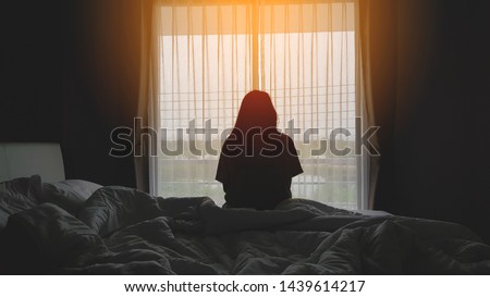 silhouette of woman sitting on the bed beside the windows with sunlight in the morning Royalty-Free Stock Photo #1439614217