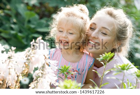 Cheerful and loving family on vacation. Emotional portrait of a happy and beautiful young mother with blond hair, hugging with a smile her funny little daughter looking at the flowers.Summer.Childhood