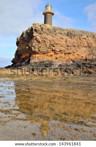 Lighthouse near to the cliff and reflexes on the water puddles in tip of Jandia, Fuerteventura, Canary islands, Spain
