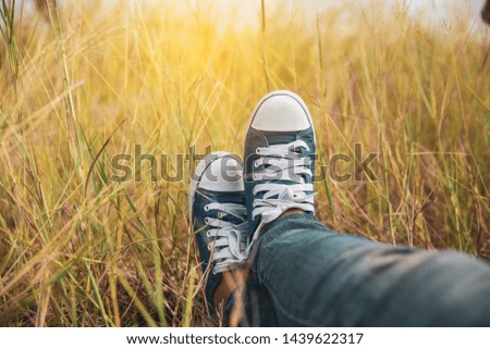 Picture of feet of woman (lonely girl),wearing white sneakers and blue jeans.Foot of female (traveler) sitting in green fields beside.Travel and success concept
