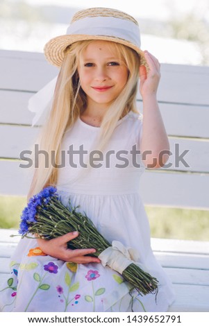 Girl with light hair in a white dress and a hat strolls along a sandy beach