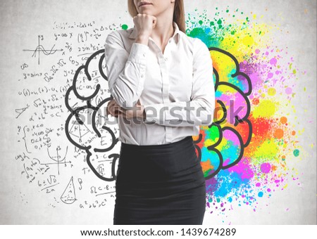 Unrecognizable pensive woman in business suit standing near concrete wall with colorful brain sketch drawn on it. Concept of brainstorming.