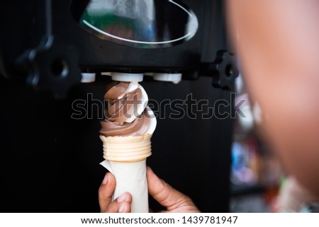 Human hand holding cone with twisted ice cream from machine