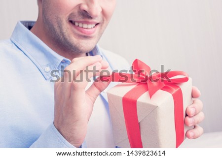 An attractive man received a birthday gift. The man smiles and opens the gift . Portrait, cropped image, closeup, toned