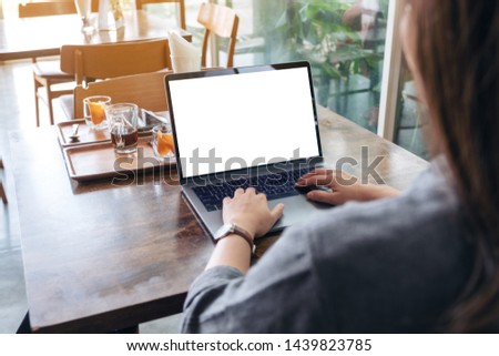 Mockup image of a woman using and typing on laptop with blank white desktop screen on wooden table 