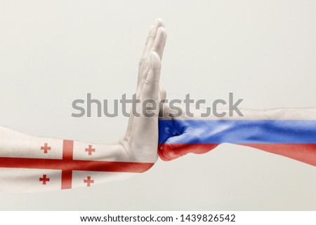 Stopping pressure. Two male hands fighting colored in Russian Federation and Georgia flags isolated on white studio background. Concept of political, economical, social aggressions, disagreement.