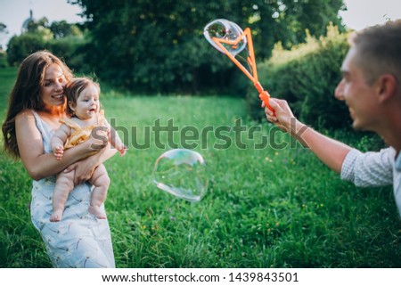 A small and very beautiful baby girl plays with her parents and bubbles on the grass