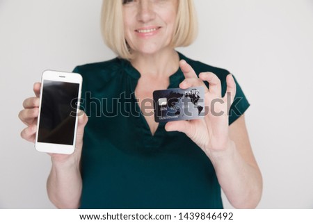 Photo of smiling adult lady with mobile and credit card in her hands.