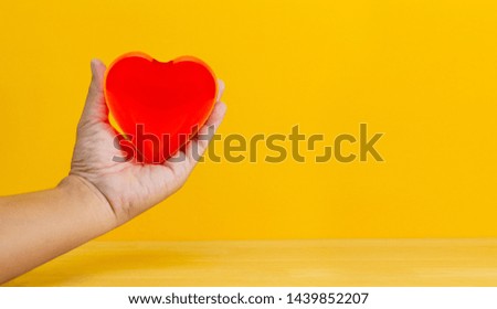 hand holding red hearton wood table and yellow background, medical and health care concept, valentine day