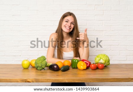 Young woman with many vegetables making phone gesture