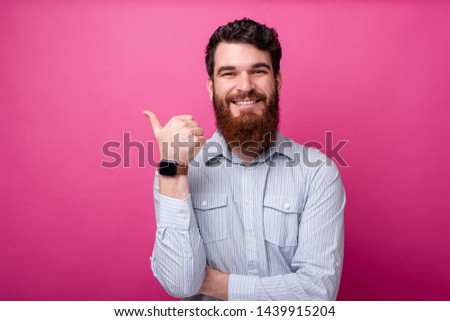 Portrait of cheerful man with beard in shirt pointing at copyspace