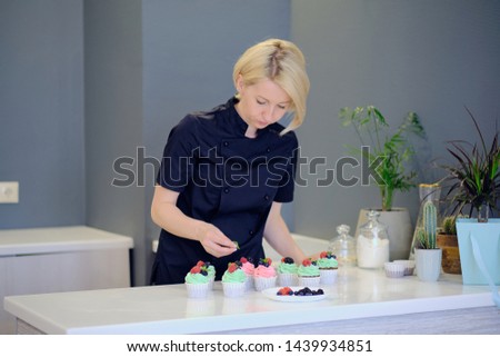 Close up of female hand topping a cupcake with refreshing mint leaf or picking it. Pastry chef woman making sweet dessert cake. Horizontal imag