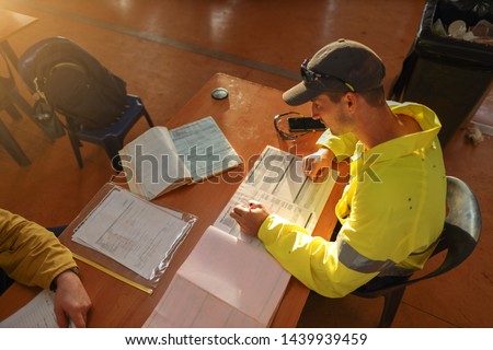 Top view of young construction gold miner worker seating writing job hazards analysis on hot work, working at height risk assessment safety control permit prior to start each shift 