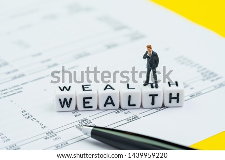 Wealth management, success investment or financial independent concept, miniature businessman standing and thinking on cube block building the word Wealth on profit and loss report with numbers.