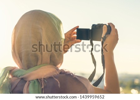 Arab Woman Photographer in a scarf taking picture using Camera on the sunset background. Halal travel concept