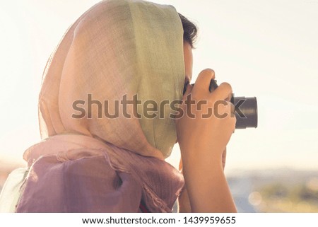 Arab Woman Photographer in a scarf taking picture using Camera on the sunset background. Halal travel concept