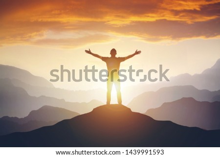 Man standing on edge of mountain feeling victorious with arms up in the air. Success, life goals, achievement concept. Royalty-Free Stock Photo #1439991593