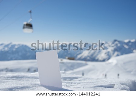 Lift pass card in snow with blurred ski-lift cable car and mountain range. Concept to illustrate winter sport admission fee