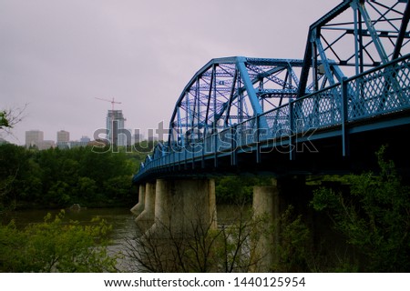The blue Riverside bridge looking over downtown Edmonton with the river flowing  below it . 