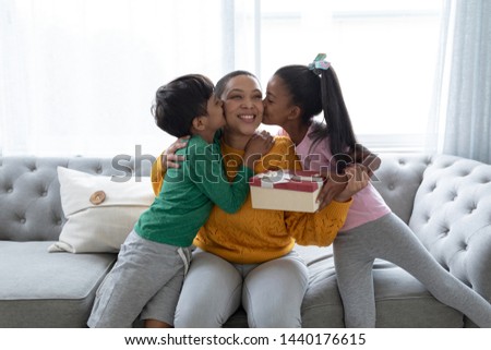 Front view of African american children congratulating mother and giving her gift box in living room at home. Social distancing and self isolation in quarantine lockdown for Coronavirus Covid19