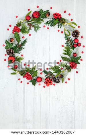 Abstract Christmas wreath with red bauble decorations, holly, pine cones, mistletoe, snow covered spruce fir and loose red berries on rustic white background with copy space.