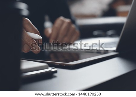 Business man hand with stylus pen touching on digital tablet screen while working on laptop computer with cup of coffee, notebook on desk, close up. Student studying online course. E-learning concept