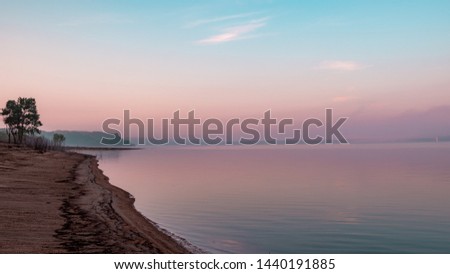 Shoreline and reflection of pink clouds on a lake. Saylorville Lake, near Polk City, Iowa, USA. Blue hour, fog in the distance, cotton candy clouds, sunrise in the Midwest.  Royalty-Free Stock Photo #1440191885
