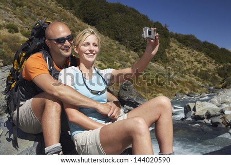 Man hugging woman as she takes their picture by river in the forest