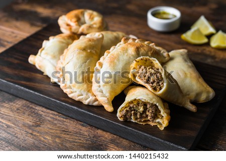 Traditional baked Argentine empanadas savoury pastries with meat beef stuffing against wooden background Royalty-Free Stock Photo #1440215432
