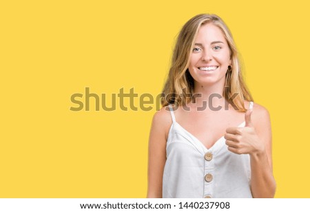 Beautiful young woman over isolated background doing happy thumbs up gesture with hand. Approving expression looking at the camera with showing success.