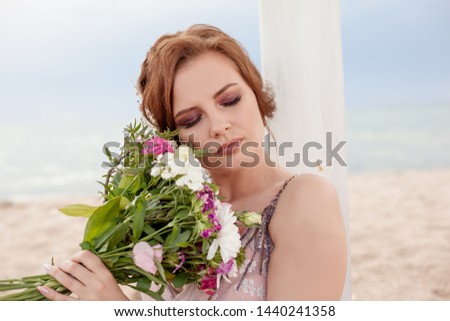 bride holds in her arms the wedding bouquet, and sit in the beach against the sea or ocean