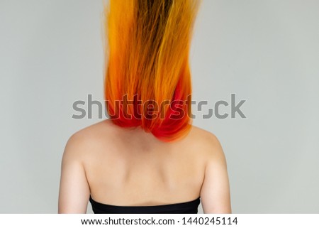 A close-up portrait photo of a fashionable hairstyle red-yellow in studio on a white background. The pretty brunette model with beautiful make-up has beautiful flowing colorful hair.
