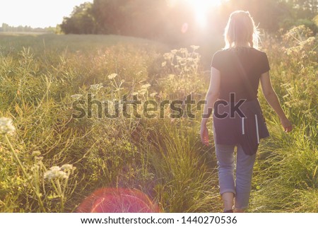 Woman walking in a field in the sunset Royalty-Free Stock Photo #1440270536