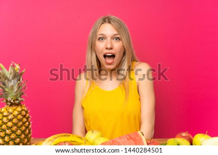 Young blonde woman with lots of fruits with surprise facial expression