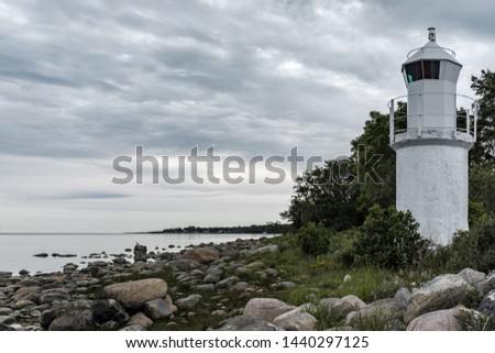 A shot of the beautiful rocky coast of the sea with a white lighthouse tower on the side and cloudy sky