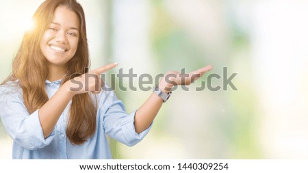 Young beautiful brunette business woman over isolated background amazed and smiling to the camera while presenting with hand and pointing with finger.