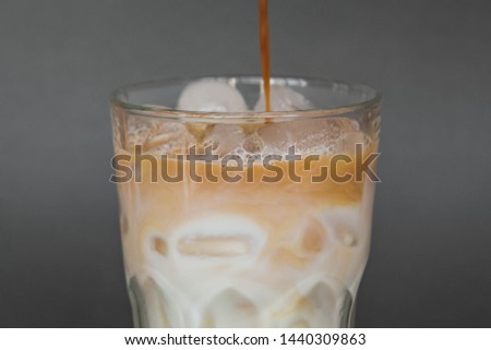 A large transparent glass filled with cold summer drink Latte with ice cooked in a third wave coffee shop is photographed on a gray, isolated background, photo for the menu