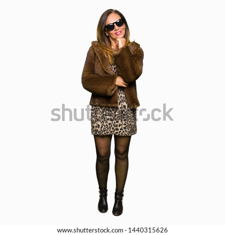 Beautiful middle age elegant woman wearing sunglasses and mink coat with hand on chin thinking about question, pensive expression. Smiling with thoughtful face. Doubt concept.