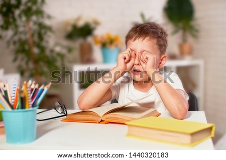 the child is tired of learning. home schooling, homework. the boy rubs his eyes from fatigue reading books and textbooks. a little boy student sitting at a table with books. vision problems Royalty-Free Stock Photo #1440320183