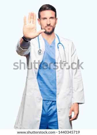 Handsome doctor man wearing medical uniform over isolated background doing stop sing with palm of the hand. Warning expression with negative and serious gesture on the face.