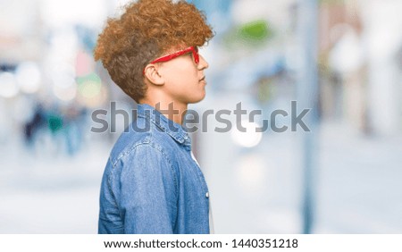 Young handsome man with afro hair wearing glasses looking to side, relax profile pose with natural face with confident smile.