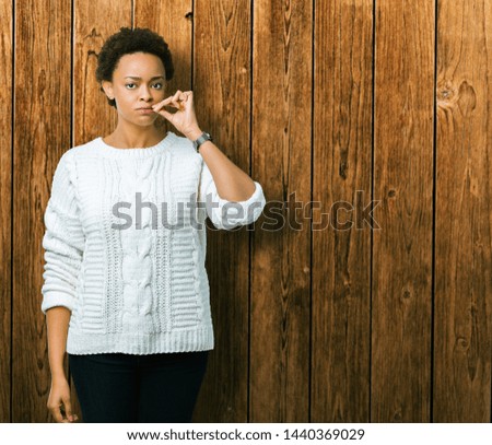 Beautiful young african american woman wearing sweater over isolated background mouth and lips shut as zip with fingers. Secret and silent, taboo talking