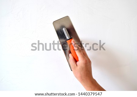 Hand with a spatula, the process of applying a layer of putty. Renovation of apartments. Repair the walls. Free space for advertising, text.