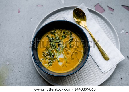 Pumpkin soup with golden spoon on gray stone background from above. Minimalism food photography concept, copyspace, top view, close up