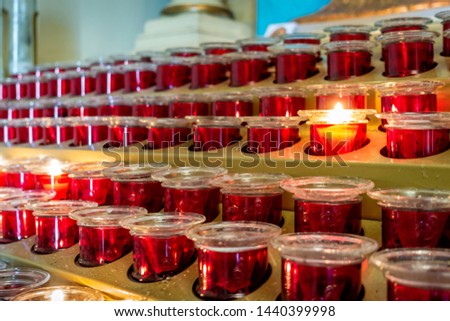 Close-up view of a series of devotional tea light candles arranged on a stand. Low-light image. Commonly seen inside churches.